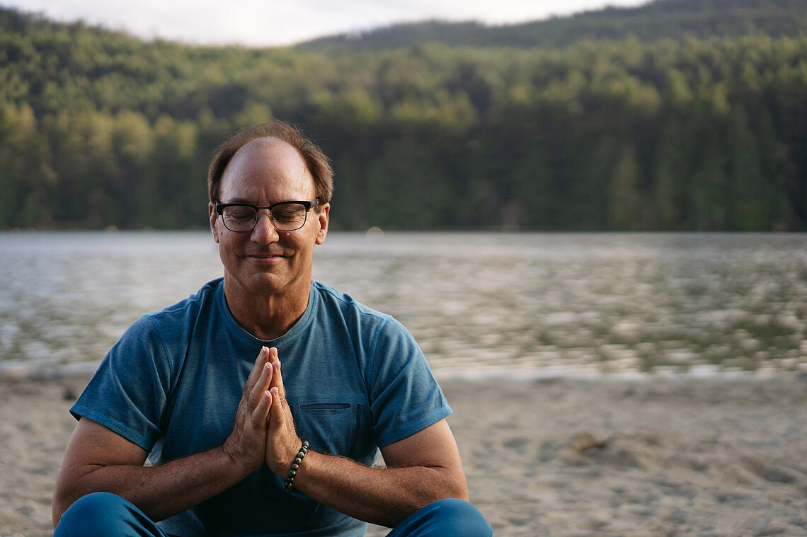 Mann meditiert am Ufer eines Sees 