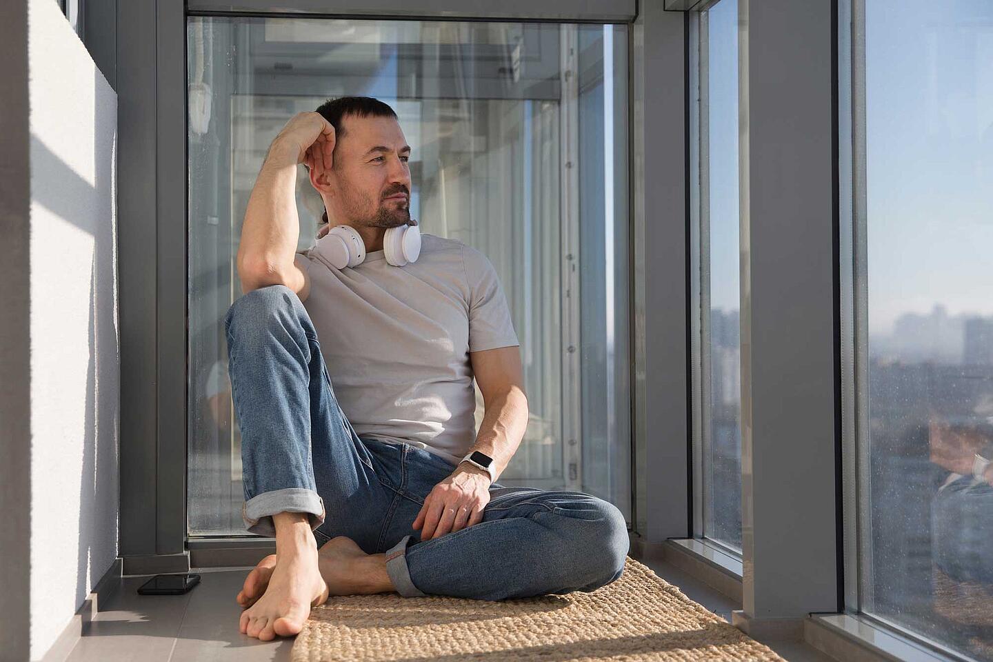 Mann mit Kopfhörern sitzt entspannt auf dem Balkon