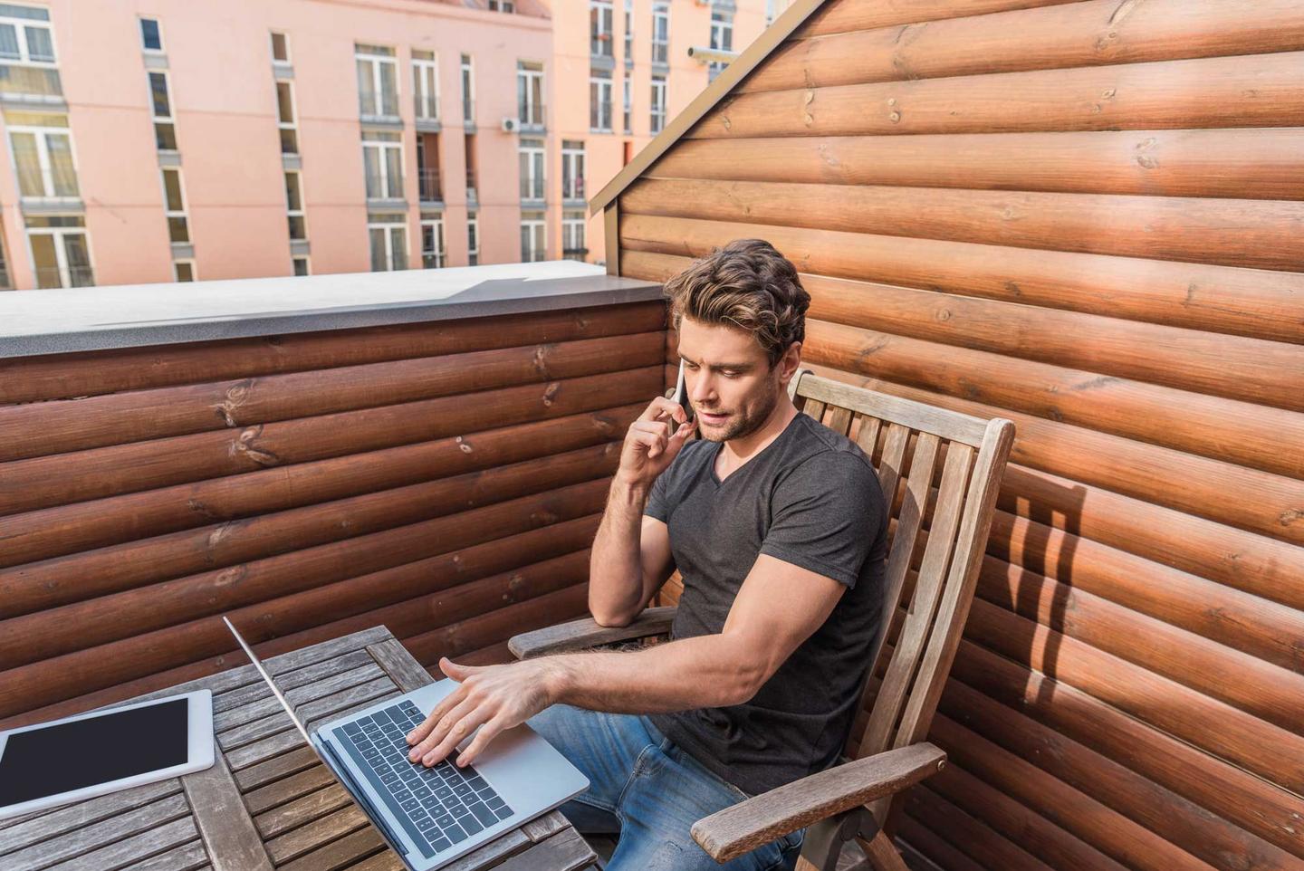 Mann im Homeoffice sitzt mit dem Laptop auf dem Balkon