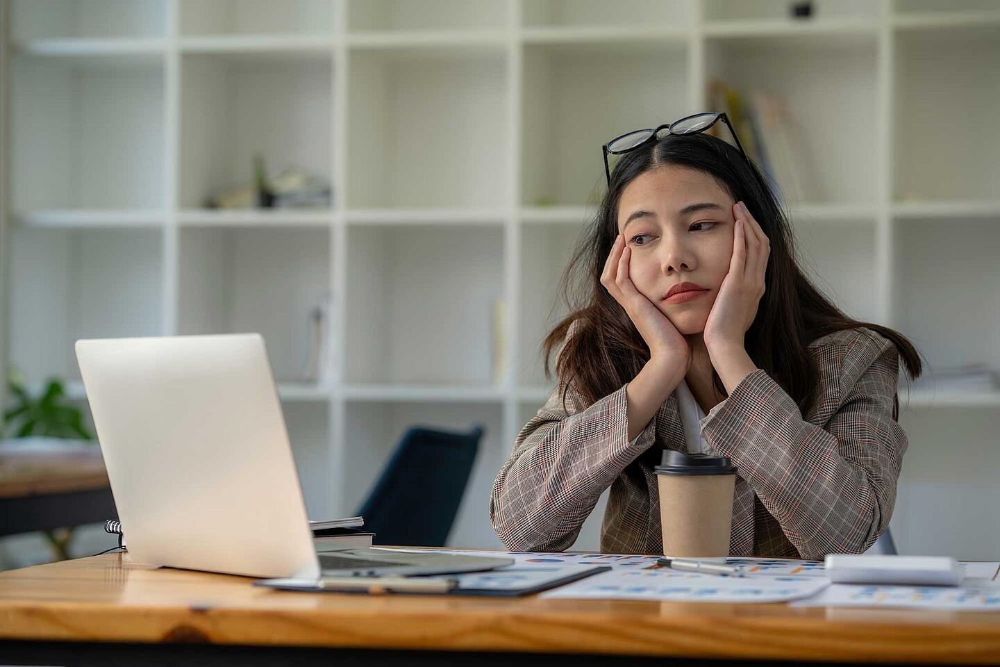 Emotionen am Arbeitsplatz: Frau sitzt müde und gelangweilt am Laptop