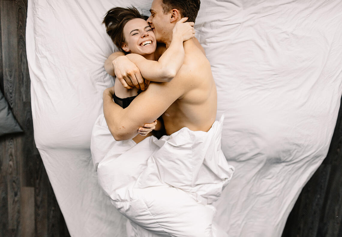 Lachendes Paar umarmt sich im Bett