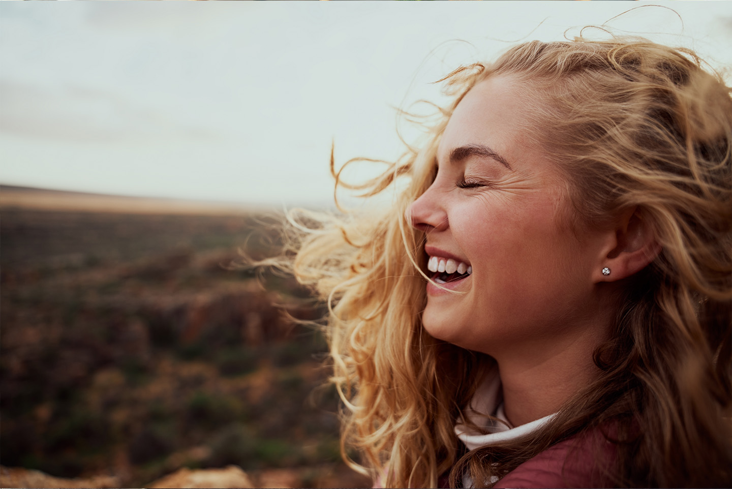 Junge Frau hält lachend ihr Gesicht in den Wind